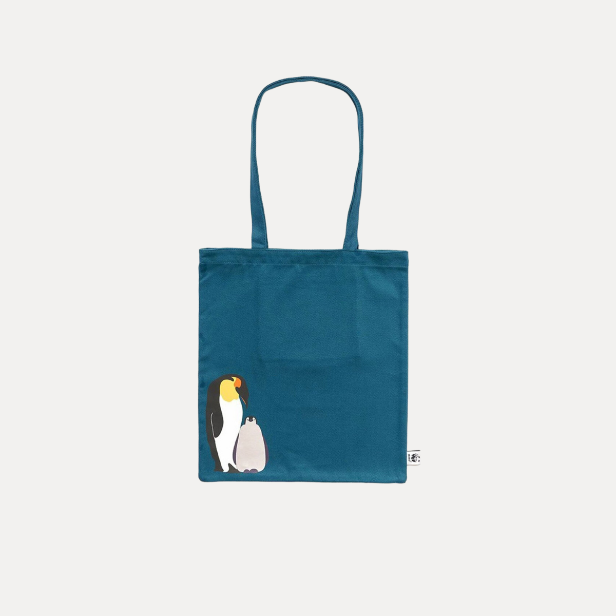 Borsa shopper di tela blu con un'illustrazione di un pinguino e un pulcino nell'angolo inferiore sinistro, su uno sfondo bianco.